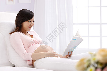卧室大半身怀孕的孕妇坐在床上看书图片