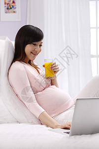 数码科技身体关注玻璃杯孕妇坐在床上看电脑图片