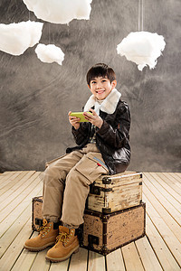小男孩坐在复古行李箱上玩游戏机图片