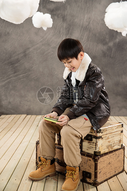 无忧无虑小男孩坐在复古行李箱上玩游戏机图片