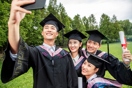 四个身穿学士服的大学生用手机自拍图片