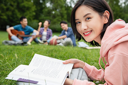 抱书女人大学生在草地上享受课余时间背景