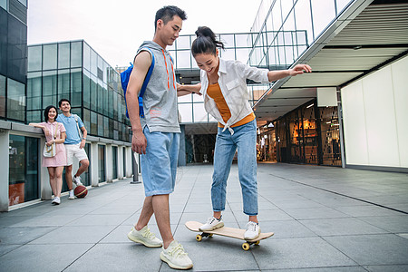 青年人帅气的大学生教女朋友滑滑板图片