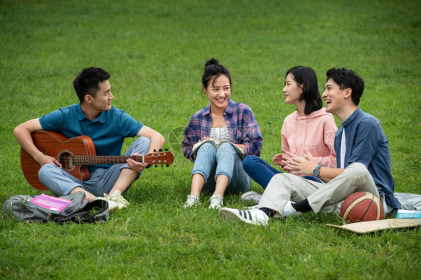 拍手男人交流快乐的大学生在草地上弹吉他唱歌图片