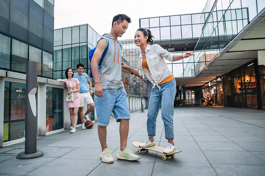 水平构图户外人帅气的大学生教女朋友滑滑板