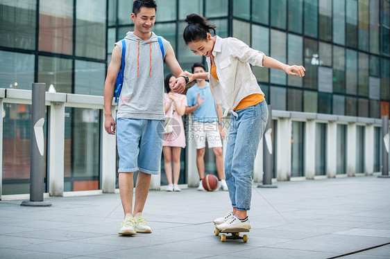 高兴的表现积极运动装帅气的大学生教女朋友滑滑板图片