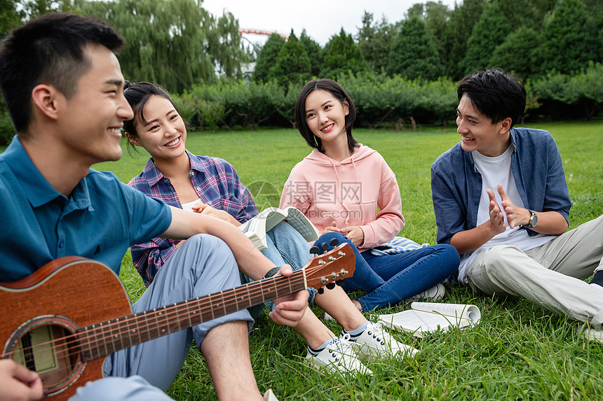 笑高等教育课外活动快乐的大学生在草地上弹吉他唱歌