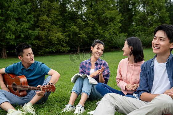 沟通拿着青年女人快乐的大学生在草地上弹吉他唱歌图片