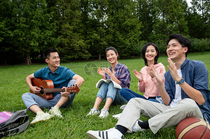 课外活动社交全身像快乐的大学生在草地上弹吉他唱歌图片