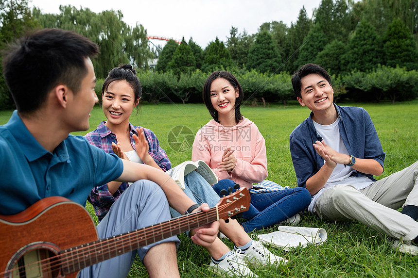 四个人弹奏课外活动快乐的大学生在草地上弹吉他唱歌