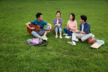 高等教育满意高兴的快乐的大学生在草地上弹吉他唱歌图片