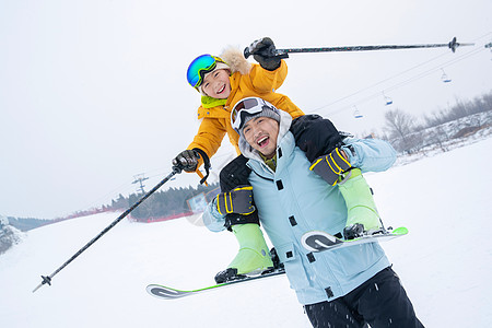 儿童滑雪滑雪场上拿滑雪杖的快乐男孩骑在父亲脖子上背景