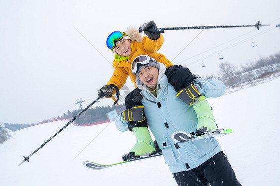 滑雪场上拿滑雪杖的快乐男孩骑在父亲脖子上图片