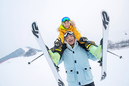滑雪场上拿滑雪杖的快乐男孩骑在父亲脖子上图片