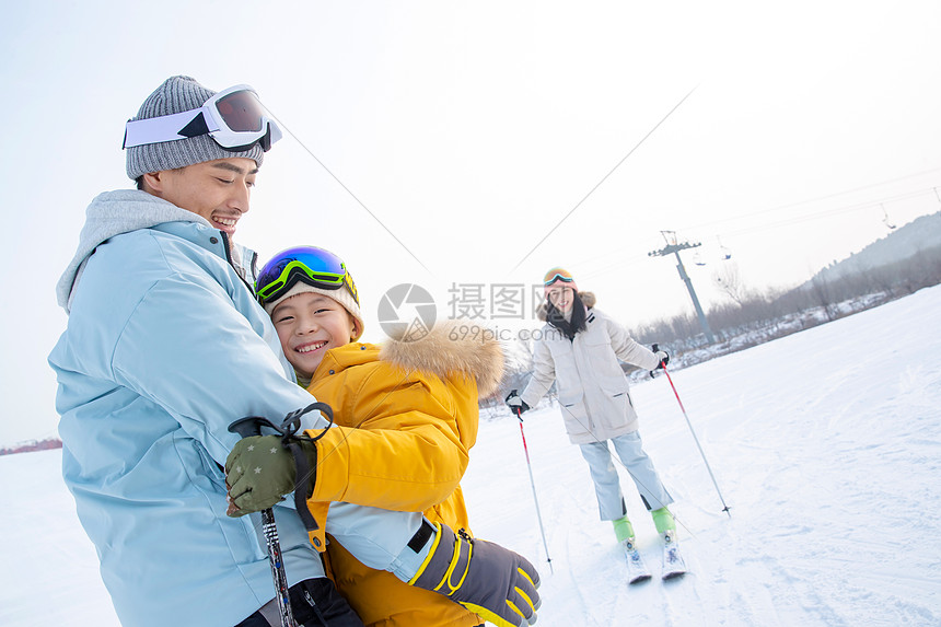 滑雪场上抱在一起的父子和滑雪的母亲图片