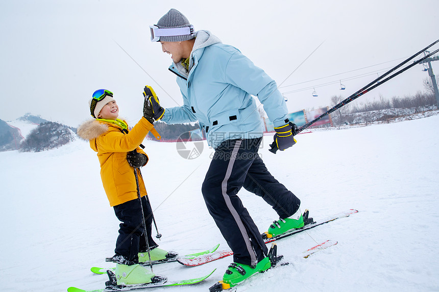 滑雪场上滑着雪击掌的快乐父子图片