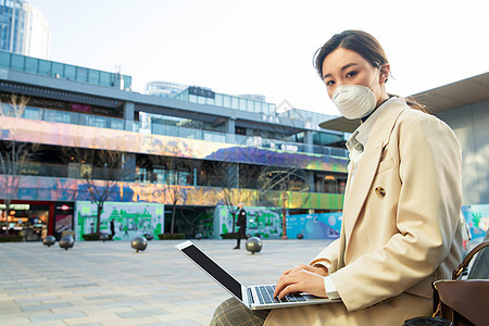 戴口罩的青年女人在户外使用电脑图片