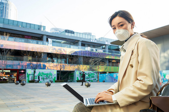 戴口罩的青年女人在户外使用电脑图片