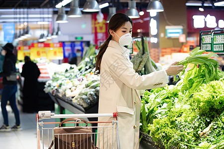 戴口罩的青年女人在超市挑选青菜图片