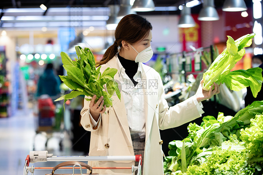 消费戴口罩的青年女人在超市购买青菜图片