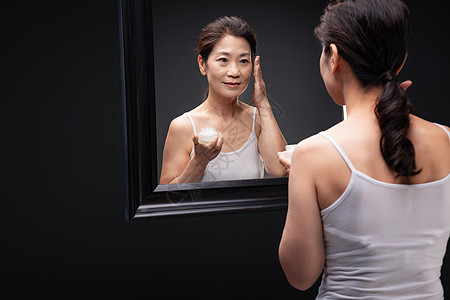 对着镜子涂抹护肤品的优雅女人图片