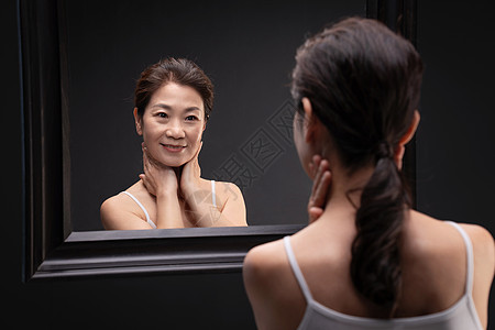优雅的中年女人对着镜子做颈部护理图片