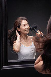 中年女人对着镜子用吹风机吹头发图片