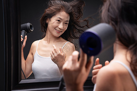 中年女人对着镜子用吹风机吹头发图片