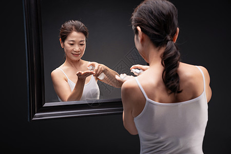 优雅的中年女人对着镜子喷爽肤水图片