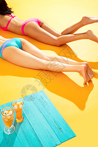 友谊黄色背景享乐比基尼闺蜜在沙滩上日光浴图片