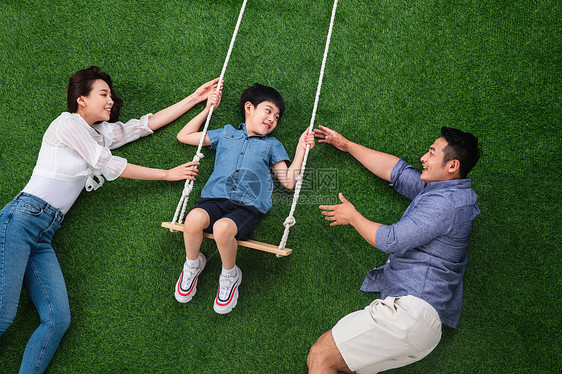 儿童爱年轻双亲幸福的一家三口在草地上荡秋千图片