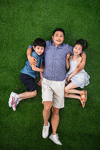 父亲搂着儿子和女儿躺在草地上背景图片