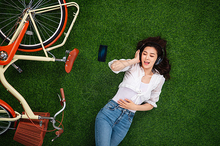 夏天穿牛仔裤躺在草地上听音乐的青年女人背景