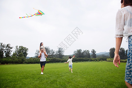 兴奋短裤青年女人快乐的一家四口在草地上放风筝图片