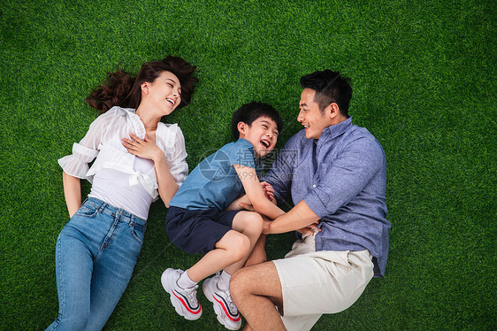 郊游亚洲8到9岁快乐的一家三口躺在草地上嬉戏图片