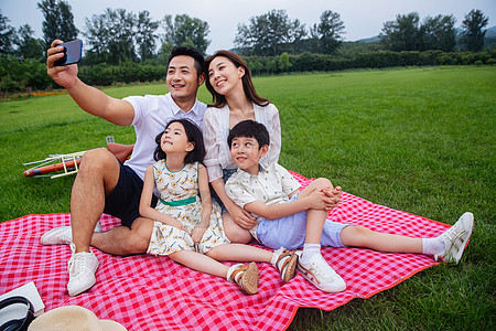 成年人宁静女儿幸福的一家四口坐在野餐垫上自拍图片