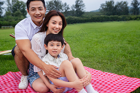 玩耍微笑双亲家庭幸福的一家三口坐在野餐垫上图片