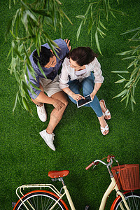 坐着青年夫妇仅成年人青年伴侣坐在草地上使用平板电脑图片