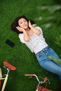 放松户外选择对焦躺在草地上听音乐的年轻女人图片