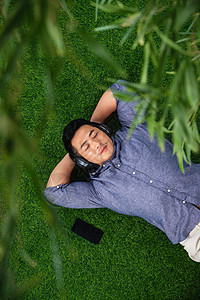 夏天音乐夏天30岁到34岁双手放在头后面躺在草地上听音乐的青年男人背景