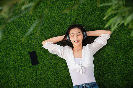 草地睡觉无忧无虑躺在草地上听音乐的青年女人背景