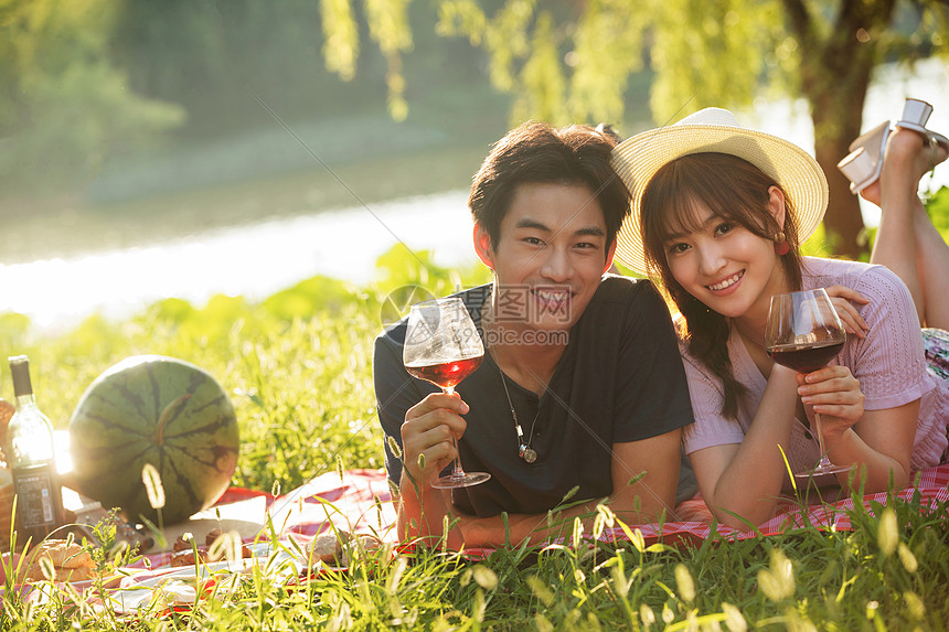 亲密趴着东亚趴在草地上喝红酒的幸福情侣图片