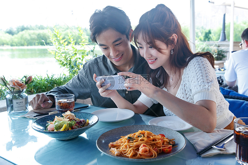 青年情侣在餐厅里用手机拍照图片
