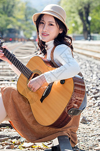 裙子旅行者自然青年女人坐在铁路边弹吉他图片