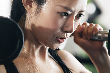 不看镜头站着汗液年轻女子在健身房练习举哑铃图片素材