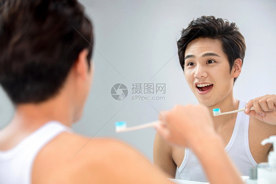 时尚反射不看镜头年轻男人对着镜子在刷牙图片