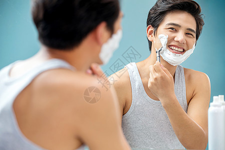 快乐的青年男人对着镜子刮胡子图片