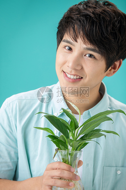 蓝色背景露齿一笑彩色图片拿着绿色植物的青年男人图片