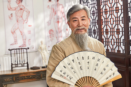注视镜头65到69岁表现积极老中医拿着扇子的肖像图片素材
