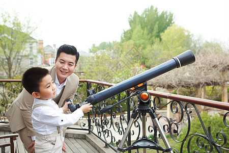 探索父亲和儿子在阳台使用天文望远镜图片